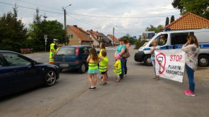 przy ulicy w Marcinkowie stoją dwa auta, radiowóz dzieci w kamizelkach odblaskowych dwoje z nich z polcjantem przy aucie