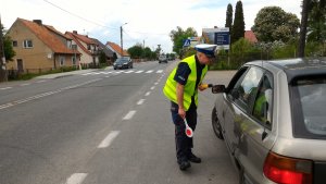 policjant w kamizelce odblaskowej kontroluje kierowcę przy aucie